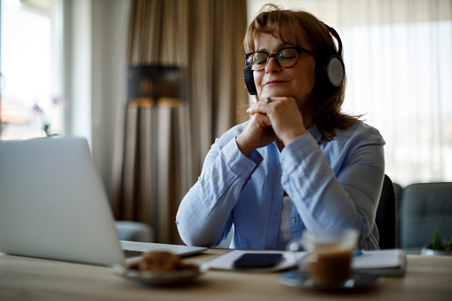 Mujer mayor sonriente con auriculares inalámbricos disfrutando de la música en casa photo