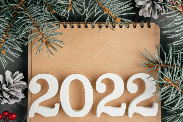 istock Happy New Year 2022. White numbers 2022 lying on folded notebook with Christmas tree branches and pine cones, copy space 1352136963