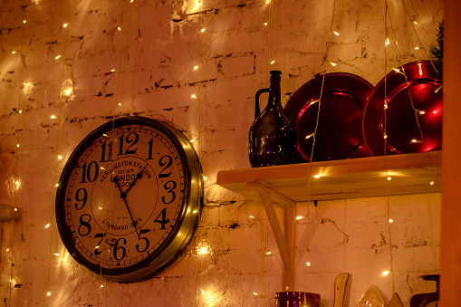 Christmas and New Year interior decoration.The white brick wall is decorated with vintage clocks and garlands. Beautiful dishes on the shelf.Selective focus.