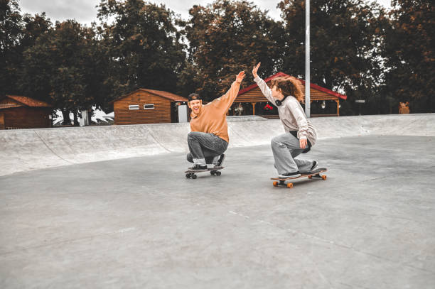 istock Guy and girl crouched on skateboards, welcomingly raising hands 1352138045