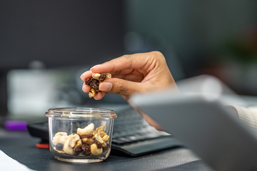 Close-up photo of a woman's hands holding nuts and raisins while using a digital tablet.