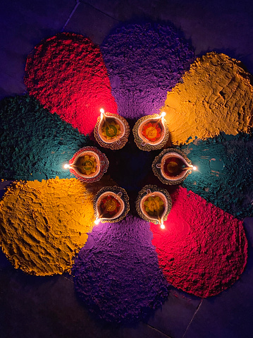 Stock photo showing an elevated view of flickering flames of oil filled diyas illuminating gulal rangoli design to celebrate Diwali the festival of lights.