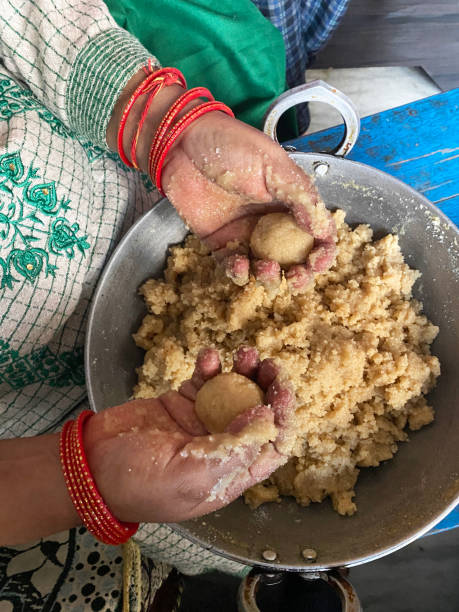 Image of ingredients for traditional motichoor ladoo sweets being moulded by woman’s hands, Indian candy ball recipe of gram (chickpea) flour (besan), ghee and sugar syrup, elevated view Stock photo showing the hands of an Indian woman moulding a mixture of gram flour (besan), ghee and sugar syrup to form into balls of motichoor ladoo sweets. human hand traditional culture india ethnic stock pictures, royalty-free photos & images