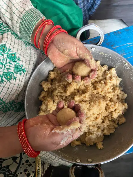 Stock photo showing the hands of an Indian woman moulding a mixture of gram flour (besan), ghee and sugar syrup to form into balls of motichoor ladoo sweets.
