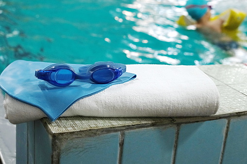 swimming pool. accessory for the pool - a towel, a rubber cap and swimming goggles on the background of the swimming track.