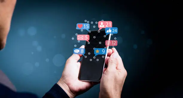 A man's hand holding a smartphone with the icons social media and social network. The concept of online marketing