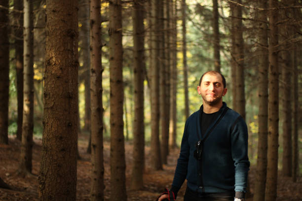 istock Smiling young man with camera in hand in forest among trees with sunlight hitting his face 1352150450