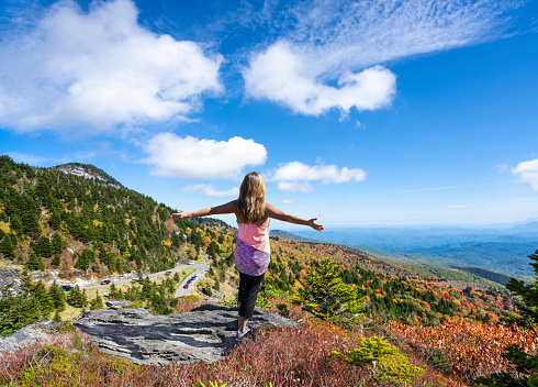 Hiker girl  with outstretched arms in autumn  mountain scenery. Woman on hiking trip with raised arms  looking at beautiful autumn mountain scenery. Grandfather Mountain State Park,  North Carolina, USA.