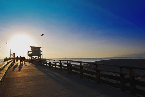 Sunset with a bright sun at Venice Beach Pier in Venice Beach, CA.  Bright sun.  Silhouettes of people and a lifeguard station.