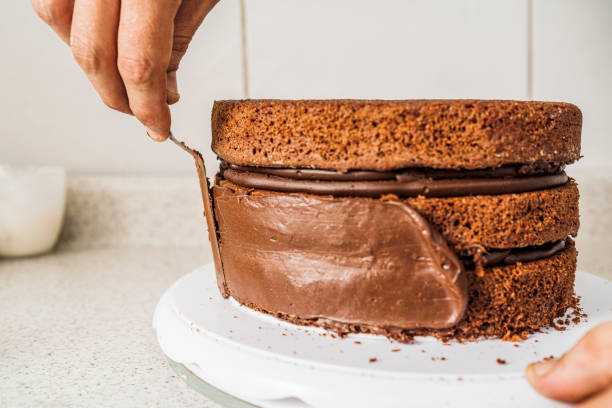 Pastry chef spreading chocolate cream on the edges of a chocolate cake indoors Pastry chef putting chocolate cream on the edges of a chocolate layer cake on a plate in a kitchen. icing stock pictures, royalty-free photos & images