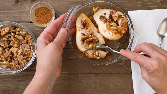 Baked pears with walnuts, honey, and cinnamon, close up on rustic background, perfect breakfast or dessert, flat lay, woman hands