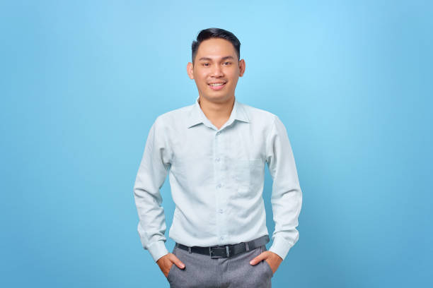 istock Smiling young handsome businessman smiling at a camera with hands in pockets on blue background 1352164300