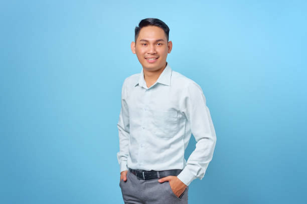 istock Smiling young handsome businessman smiling at a camera with hands in pockets on blue background 1352164303