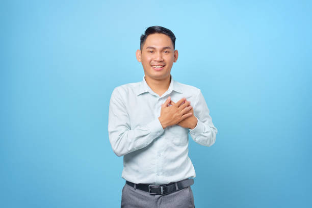 istock Thankful young handsome businessman keeping both palms on a chest on blue background 1352164422