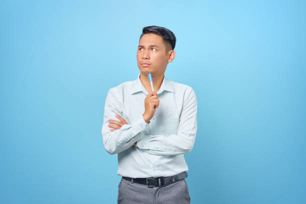 istock Serious young handsome businessman thinking about something and holding pen on blue background 1352164496
