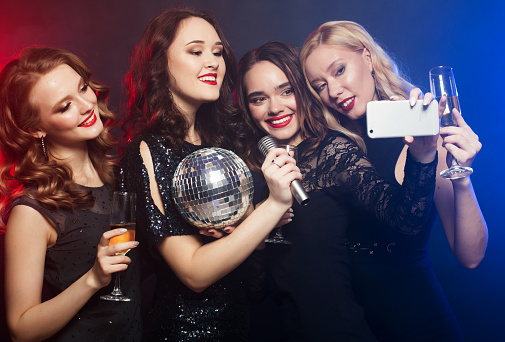 Group of glamour women in luxury black dresses drinking champagne and having fun with karaoke, selfie and happy time.