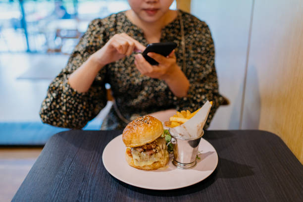 young asian woman taking photo of her burger and fries meal before eating - gourmet enjoyment food freshness imagens e fotografias de stock