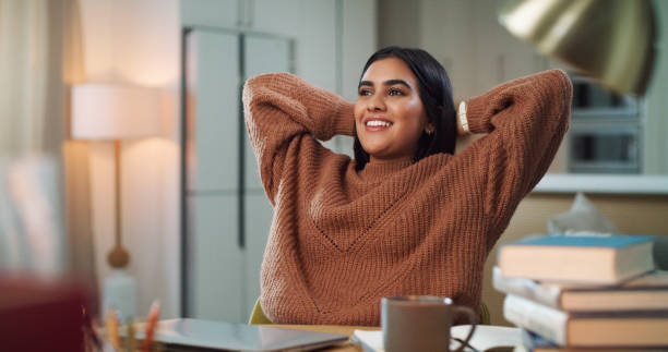 foto de una joven sentada con las manos detrás de la cabeza mientras estudiaba en casa - acabar fotografías e imágenes de stock