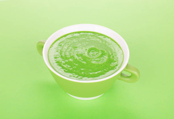 A bowl of green cream soup. It is located on a green surface. Close-up.