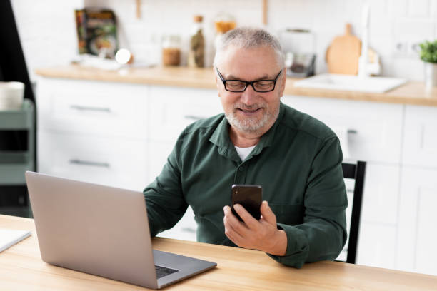 istock Senior man messaging with phone sitting at a table in a home office 1352187978