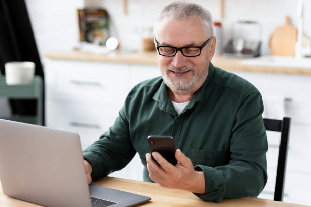 istock Senior man messaging with phone sitting at the table in the home kitchen 1352187985