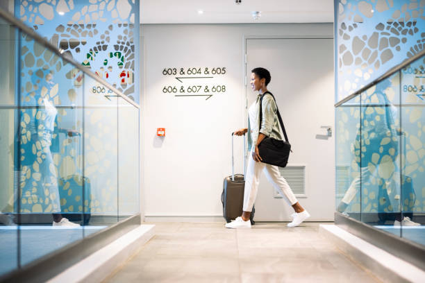 Young woman walking with wheeled luggage in hotel corridor Young woman walking with wheeled luggage in hotel corridor guest stock pictures, royalty-free photos & images