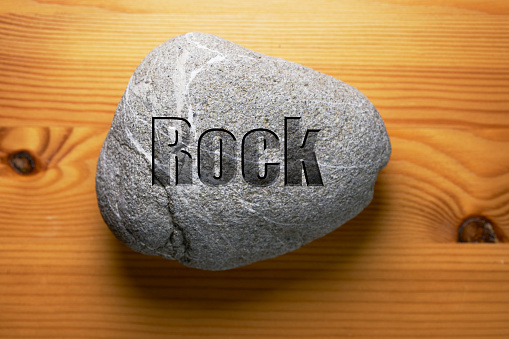 ROCK engraved with the word ROCK on a wood background