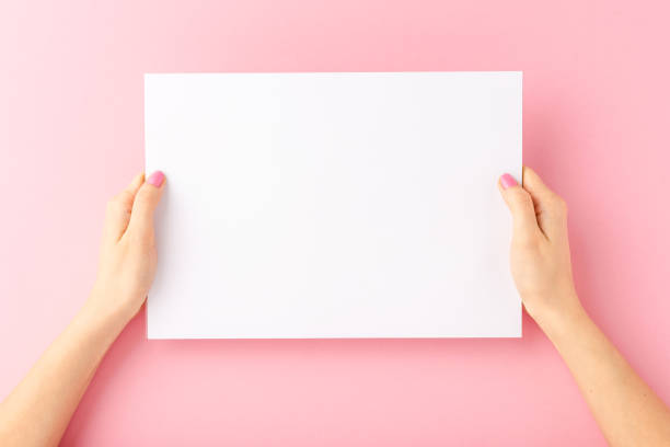 istock Woman’s hands showing white paper with copyspace on pink background. Close up 1352192232