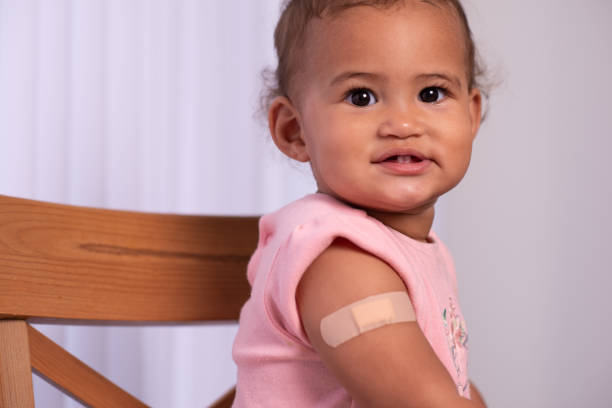 An adhesive bandage on an upper arm with the smile. Baby girl with band-aid patch on her upper arm. stock photo