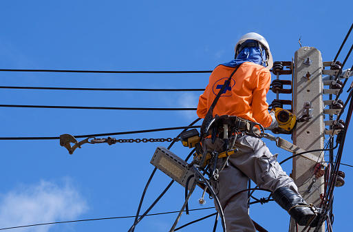 Electricista con equipos de seguridad y varias herramientas de trabajo está instalando líneas de cables y sistema eléctrico en poste de energía eléctrica contra cielo azul photo