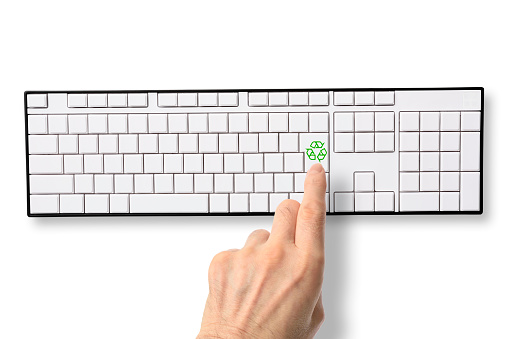 Close-up of human hand pushing blank computer keyboard with green recycling symbol, on white background. \nRecycling concepts.