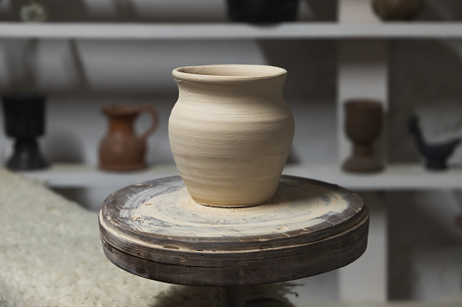 White clay pot stands on a pottery wheel, closeup
