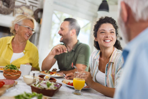 Happy adult offspring talking to their parents during a meal at dining table. Happy couple talking to senior couple during breakfast in dining room. Copy space. Focus is on mid adult couple. father in law stock pictures, royalty-free photos & images