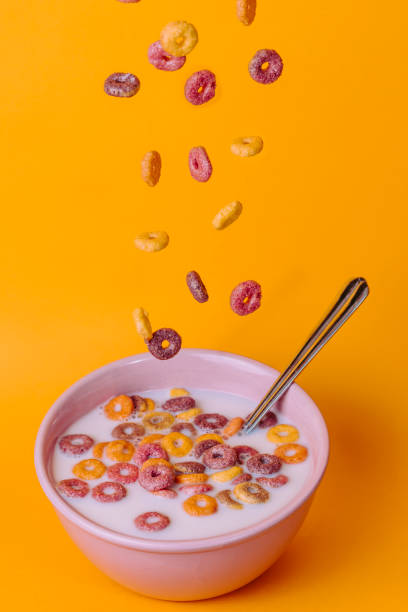 istock Colored cereals falling in a pink bowl with milk with yellow background. 1352203193