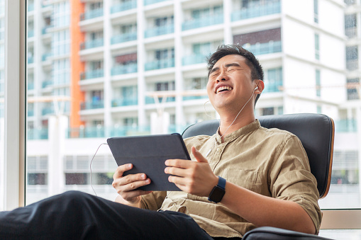 Hombre sentado en un sofá riendo a una tableta en la sala de estar photo