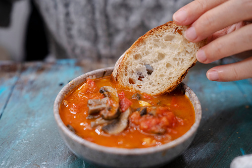 dipping a slice of baguette into stewed beef with tomato sauce