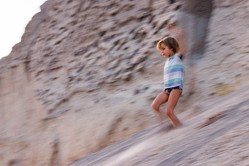 Cute little boy having fun while running down the sand dune during summer day in blurred motion. Copy space.