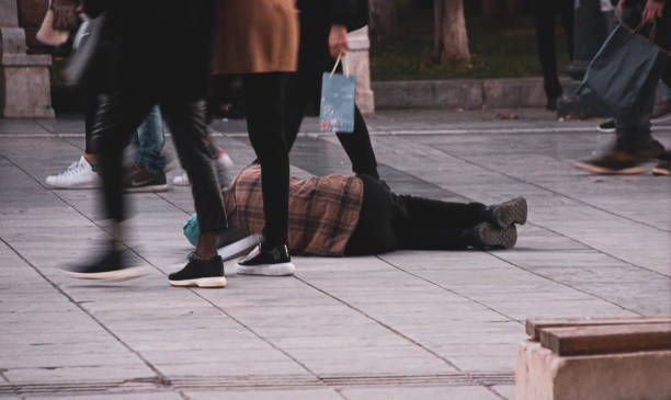 Homeless lying down at Syndagma Square. Pedestrians walking by ignoring him. Athens, Greece stock photo