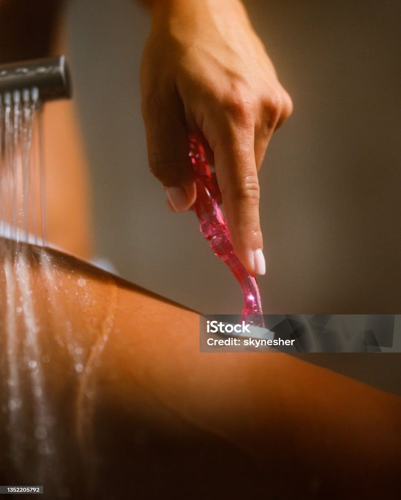 Woman shaving her leg in the bathroom. Close up of unrecognizable woman shaving her leg during a shower in the bathroom. Shaving Stock Photo