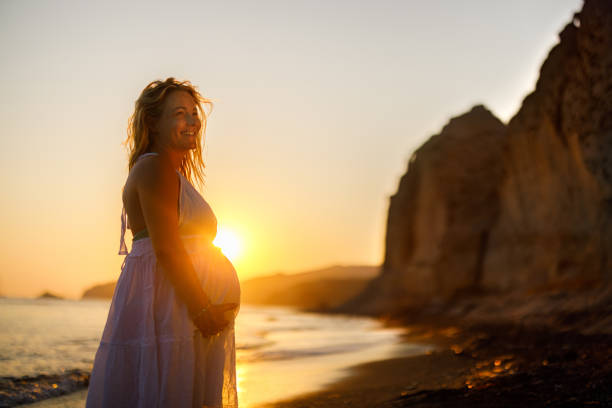 happy pregnant woman enjoying on the beach at sunset. - dress human pregnancy young women women imagens e fotografias de stock