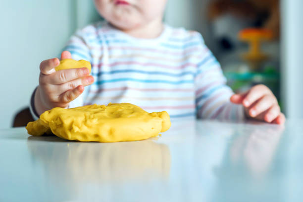 toddler boy playing yellow plasticine play-doh in playroom close-up and copy space.. - playdoh imagens e fotografias de stock