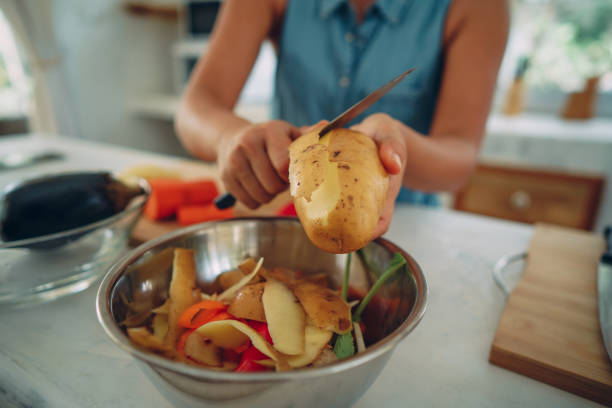 Woman's hand peeling a potato and putting a skin into a bowl for recycling.