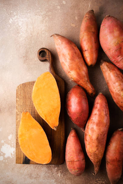 sweet potato on a brown background. exotic food. a fresh crop of vegetables. raw sweet potato. organic food - zoete aardappel fotos stockfoto's en -beelden