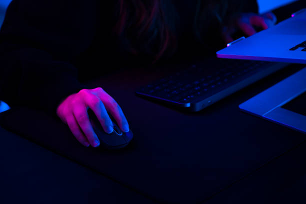 close-up of a woman's hand holding a white wired computer mouse on a wooden desk with a red glow from the LED light remote work freelancing ergonomic workspace setup technology office and productivity