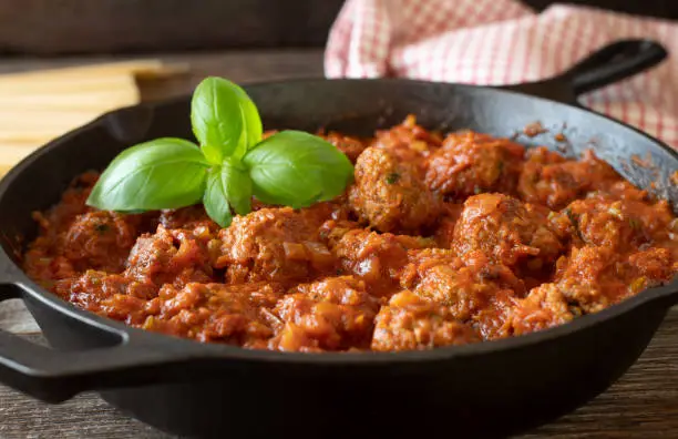 Traditional fresh and homemade cooked meatballs in a delicious vegetable, tomato sauce. Served in a cast iron pan or skillet on wooden table. Closeup and front view