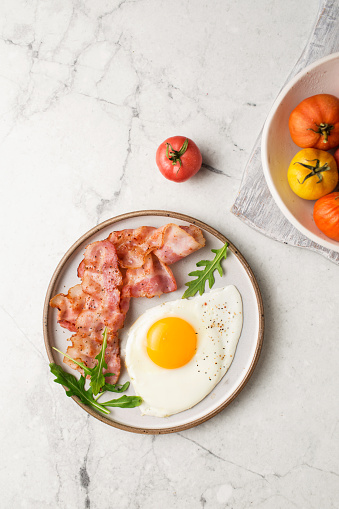English breakfast. Egg and fried bacon. A cup with tomatoes. Serving breakfast on a marble table. Fried egg.