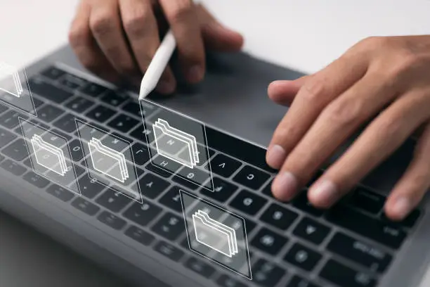 Photo of Paperless workplace concept based on e-documents. On a virtual screen, a businessman works on a laptop computer keyboard with electronic document icons.