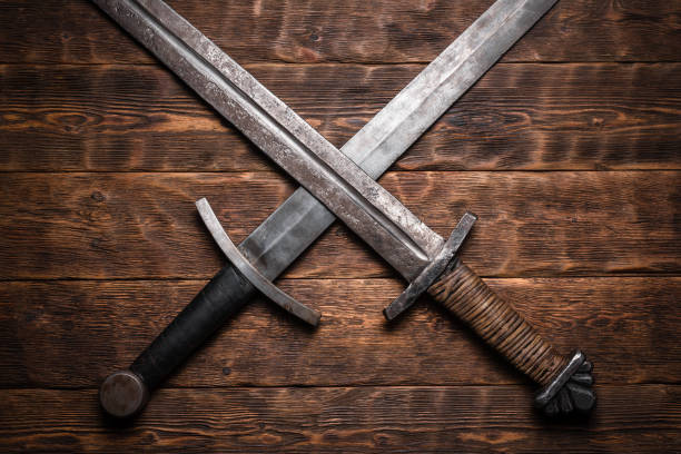Medieval knight. Two crossed swords on the old wooden table flat lay background. cross swords stock pictures, royalty-free photos & images