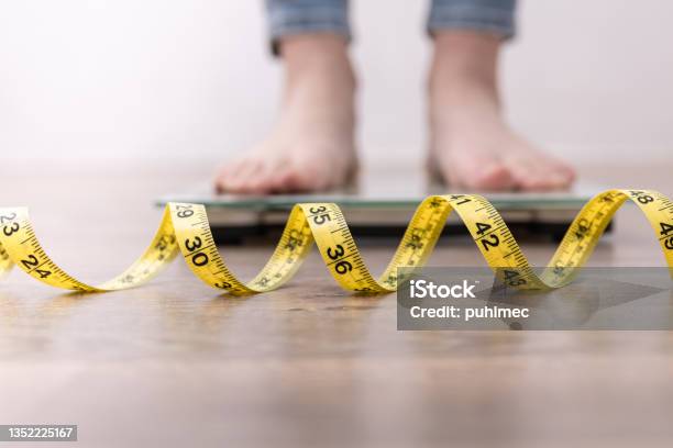 Female Leg Stepping On Weigh Scales With Measuring Tape Stock Photo - Download Image Now