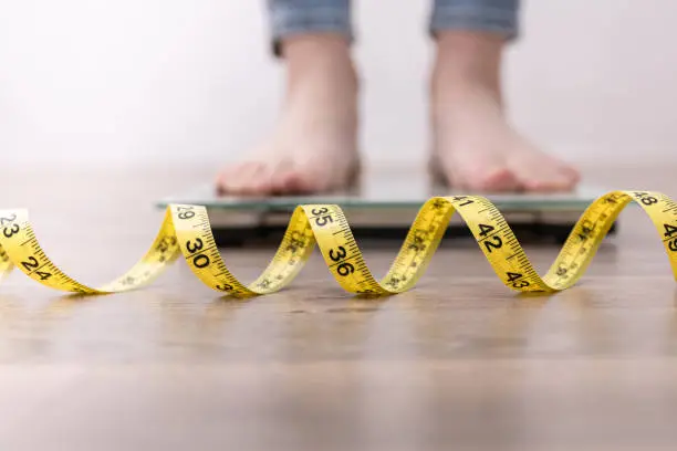 Photo of Female leg stepping on weigh scales with measuring tape.